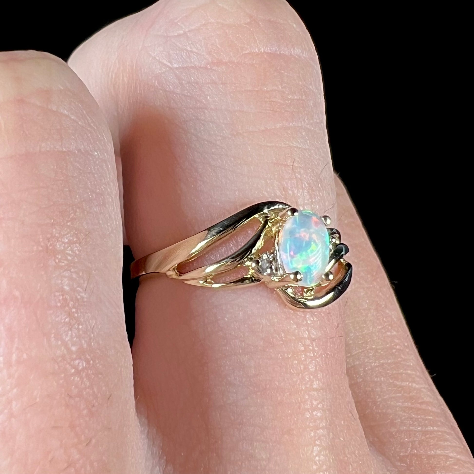 A yellow gold ring mounted with two diamond accents and an oval cut lab created opal.  The opal has bright red colors.