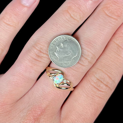 A yellow gold ring mounted with two diamond accents and an oval cut lab created opal.  The opal has bright red colors.