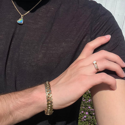 A yellow gold ring featuring two crossing, alternating lines of round cut synthetic opals.  In the middle is a larger oval cut synthetic opal.