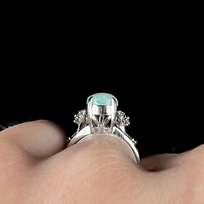 A platinum filigree ring mounted with a blue-green crystal opal and diamond accents.