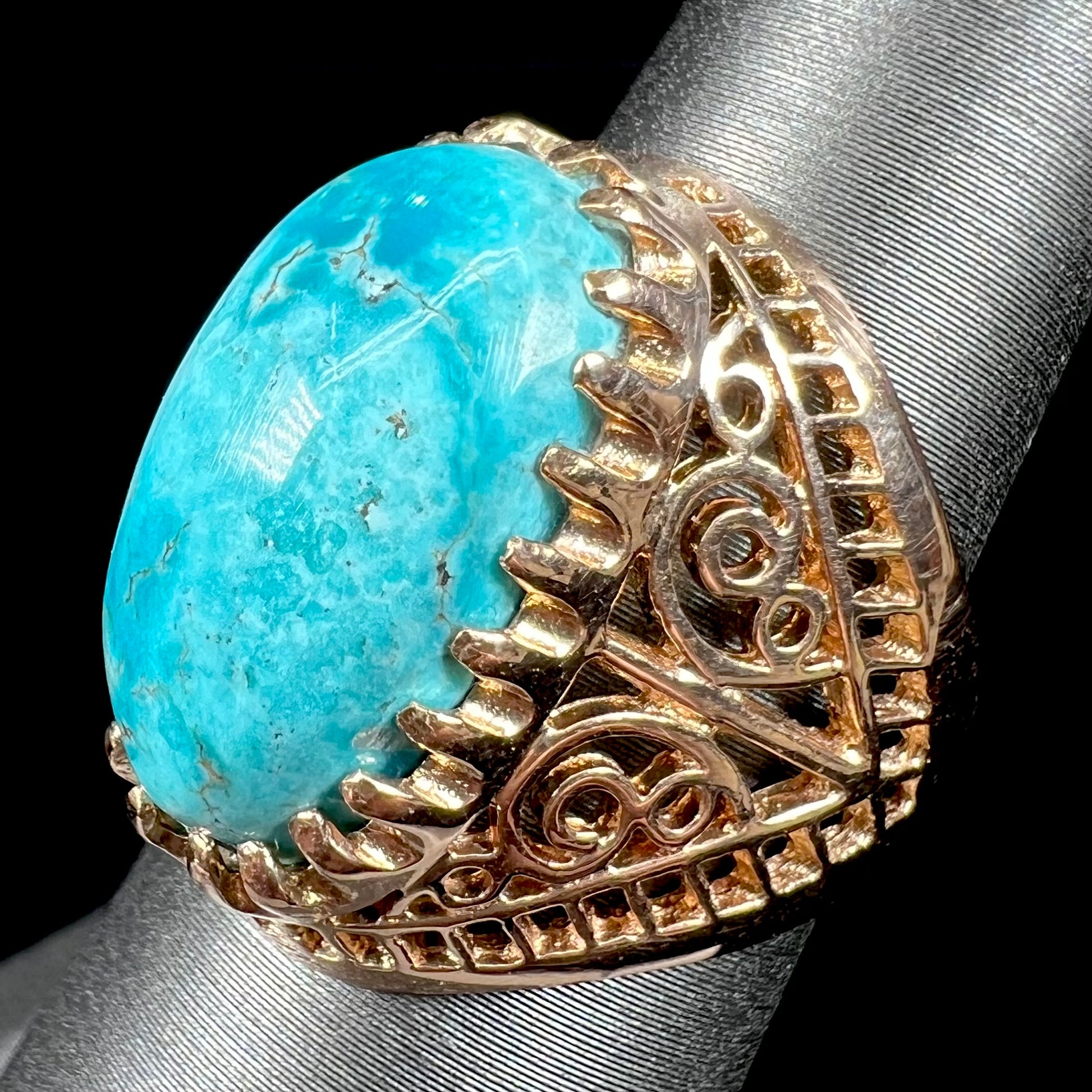 A yellow gold filigree style ring mounted with an oval Pilot Mountain turquoise stone.