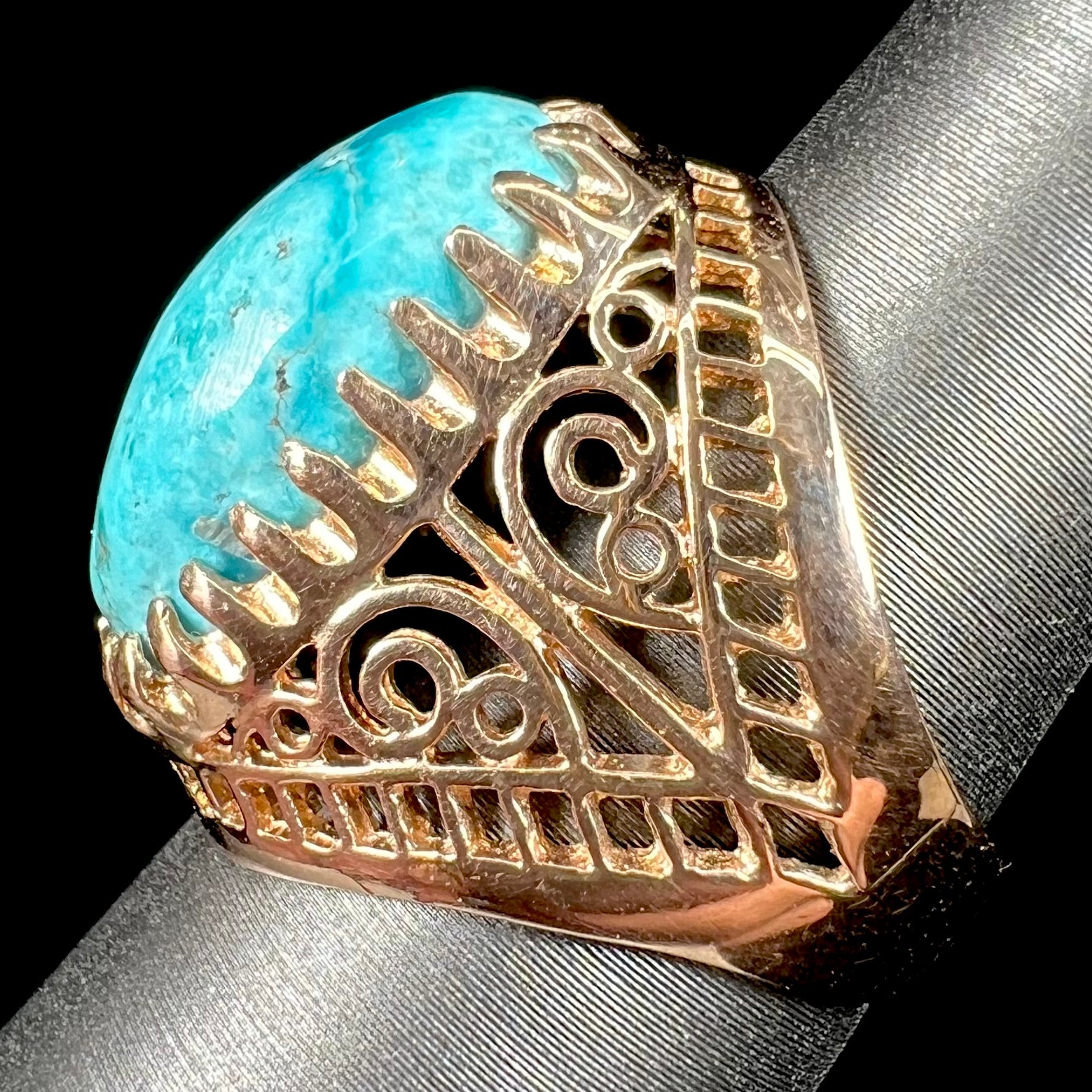 A yellow gold filigree style ring mounted with an oval Pilot Mountain turquoise stone.