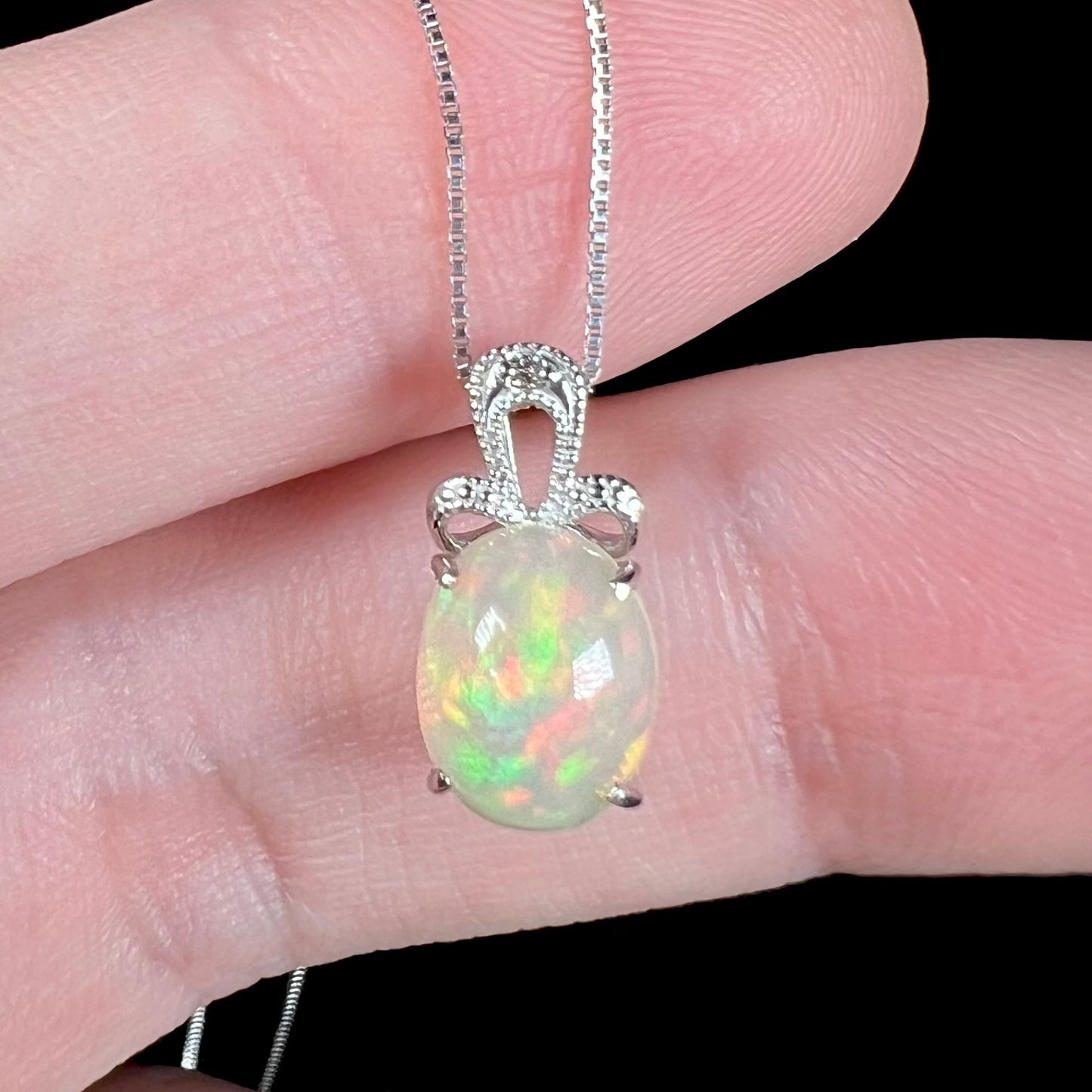 An oval cut Ethiopian opal mounted in a diamond-accented, 18 karat white gold pendant on a box chain.