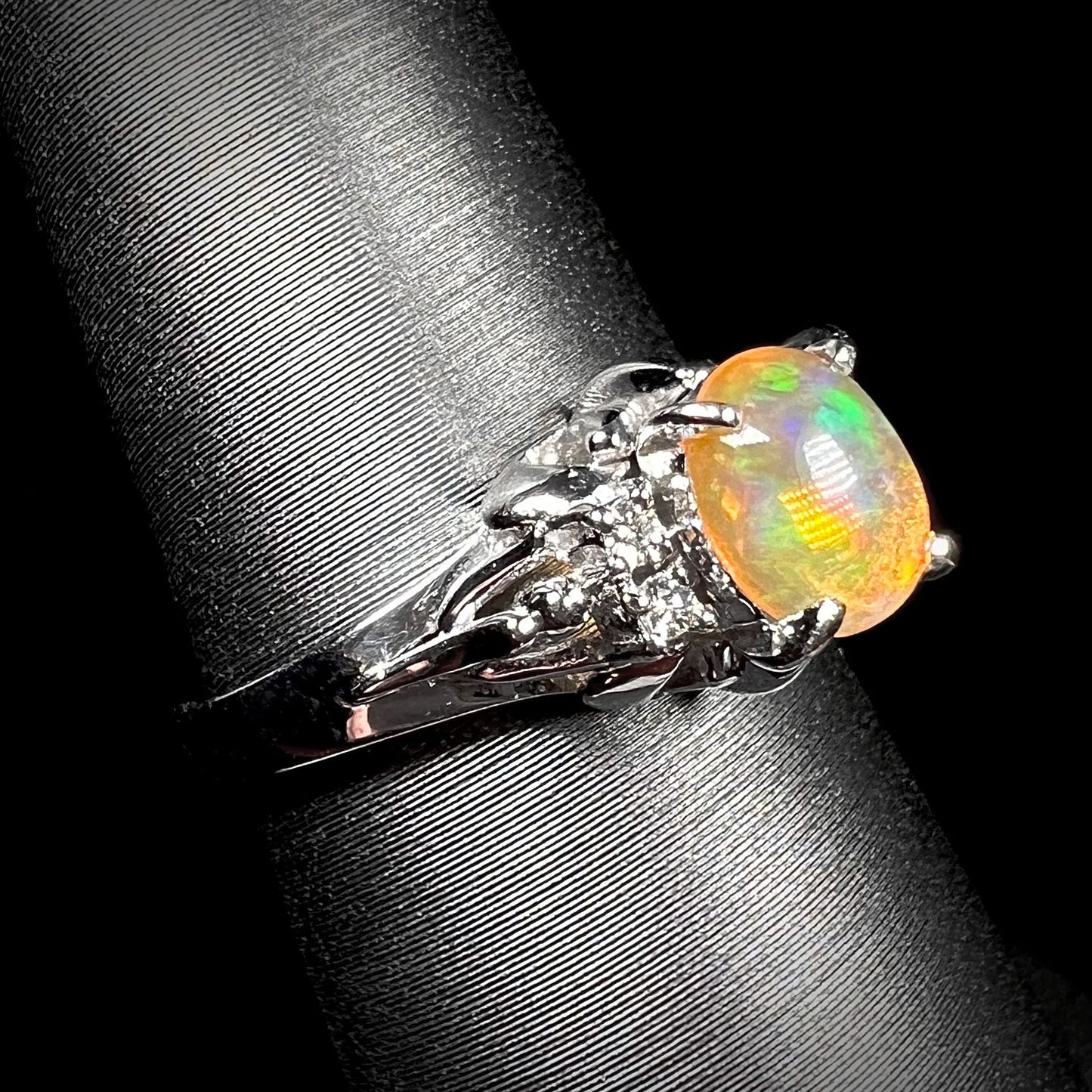 A platinum, diamond accented ring prong-set with an oval cabochon cut Mexican fire opal.