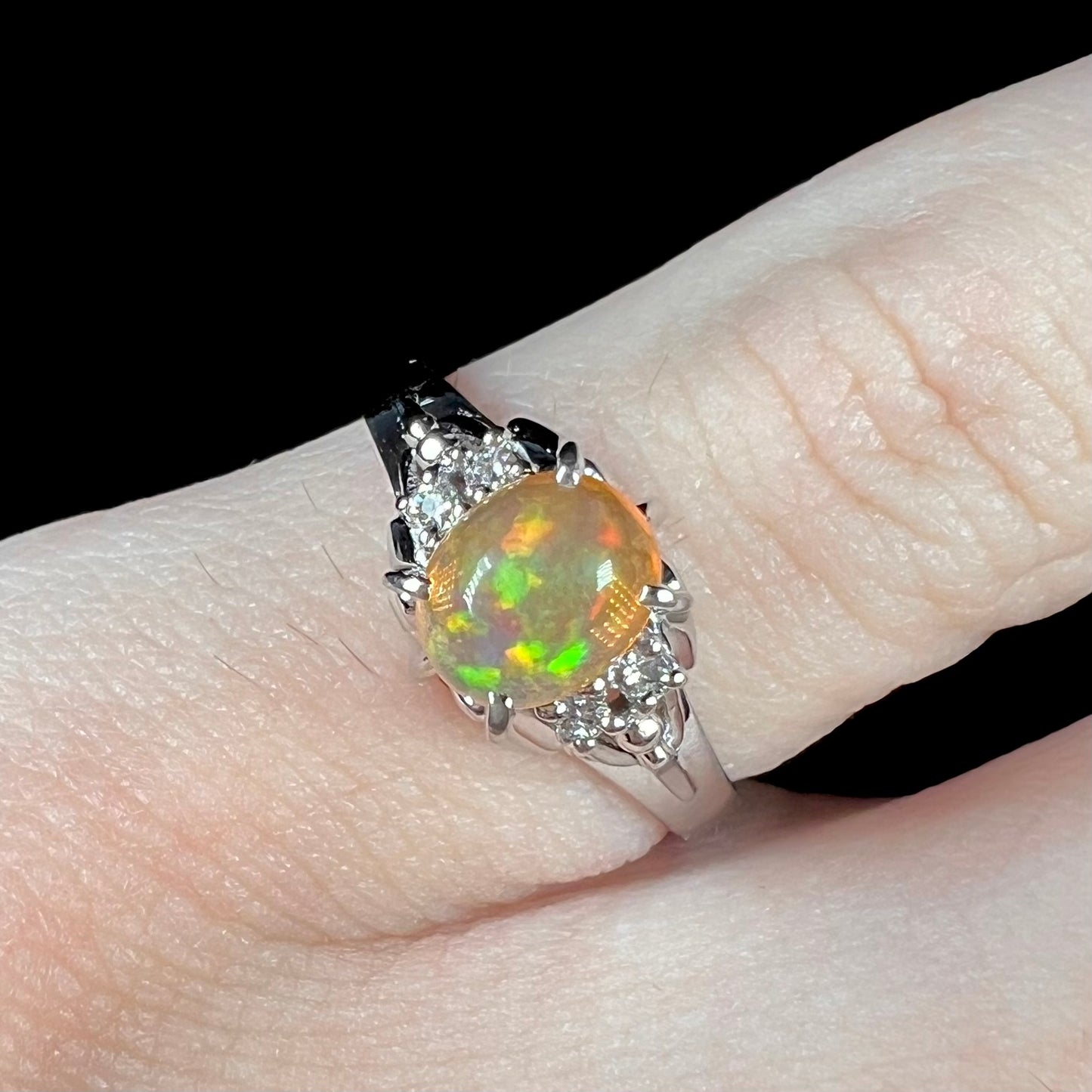 A platinum, diamond accented ring prong-set with an oval cabochon cut Mexican fire opal.