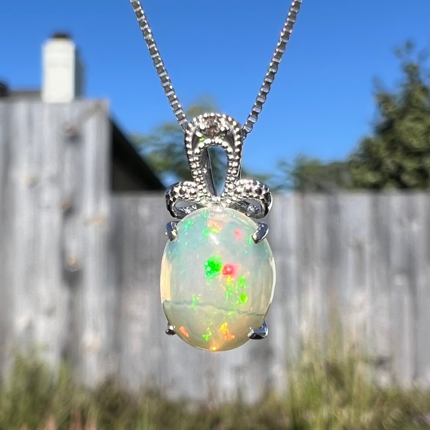 An oval cut Ethiopian opal mounted in a diamond-accented, 18 karat white gold pendant on a box chain.