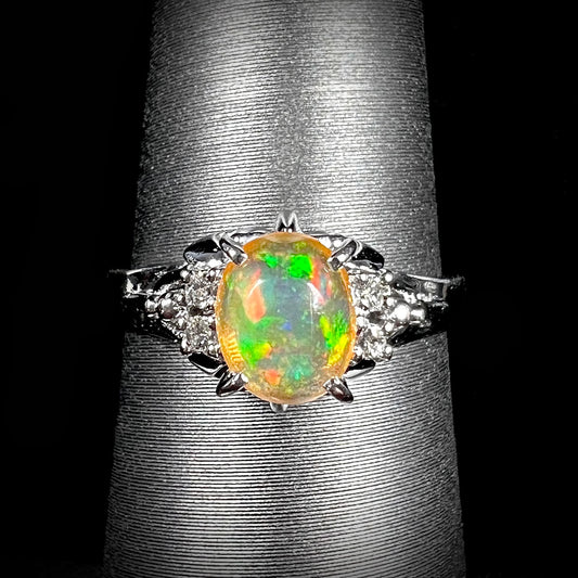 A platinum, diamond accented ring prong-set with an oval cabochon cut Mexican fire opal.