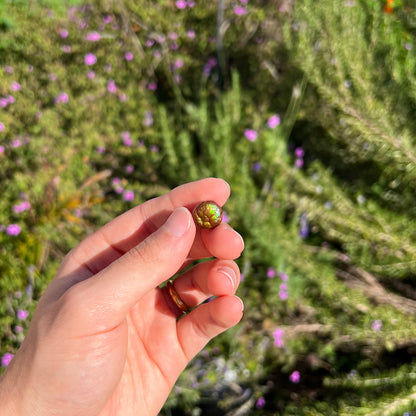 An iridescent green, yellow, and red Mexican fire agate stone.  The stone is an off-round cabochon.