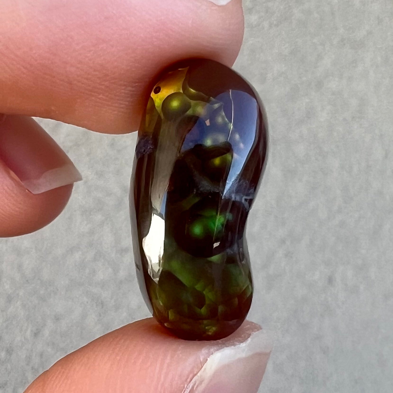 A loose, cabochon cut fire agate gemstone.  The stone resembles a foot with a green heel and yellow toes.