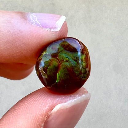 An iridescent green, yellow, and red Mexican fire agate stone.  The stone is an off-round cabochon.