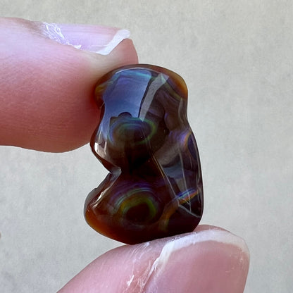 A polished, freeform shaped fire agate stone.  The stone is purple, green, and blue with red and yellow banding.