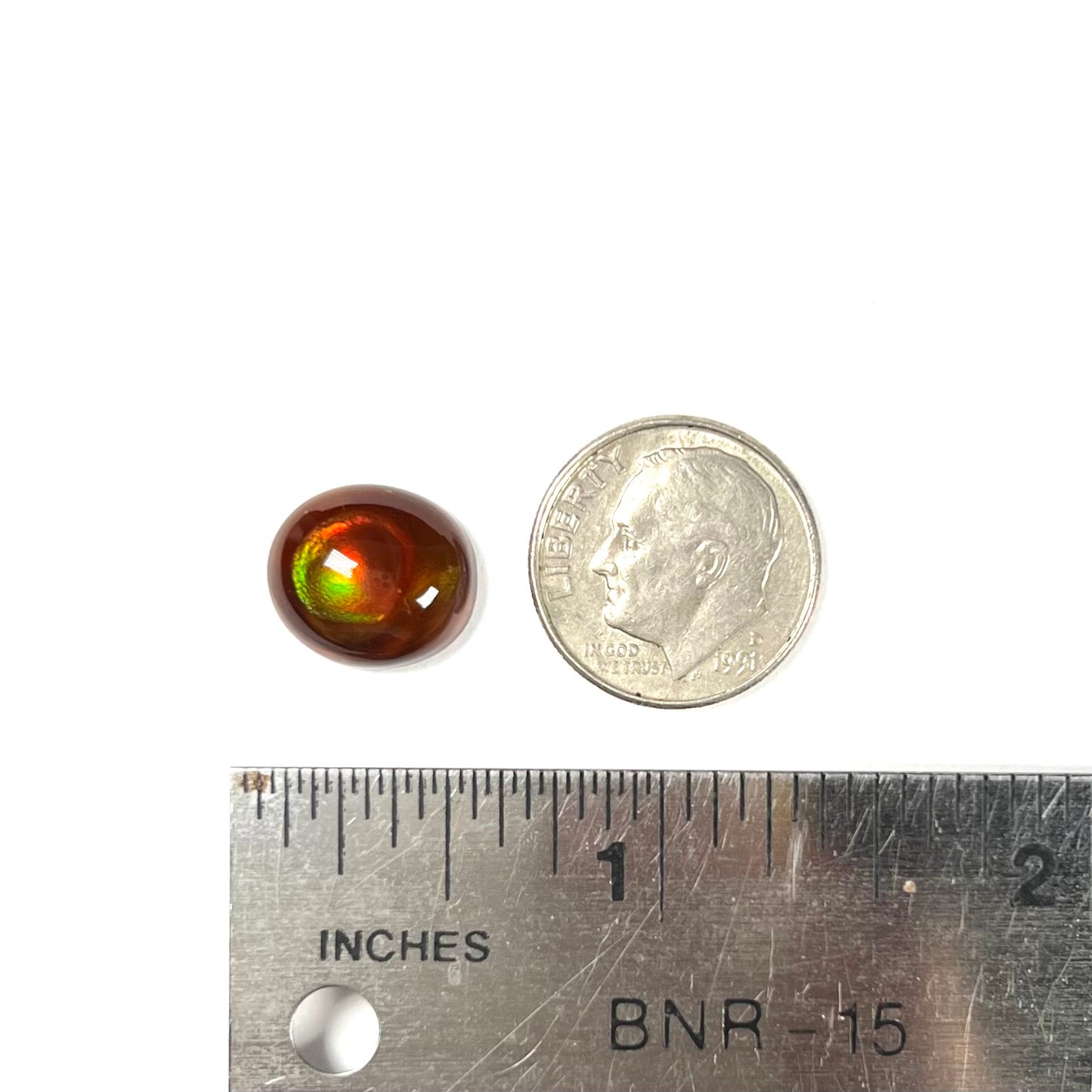 A loose, oval cabochon cut fire agate stone that has red and green colored iridescence.