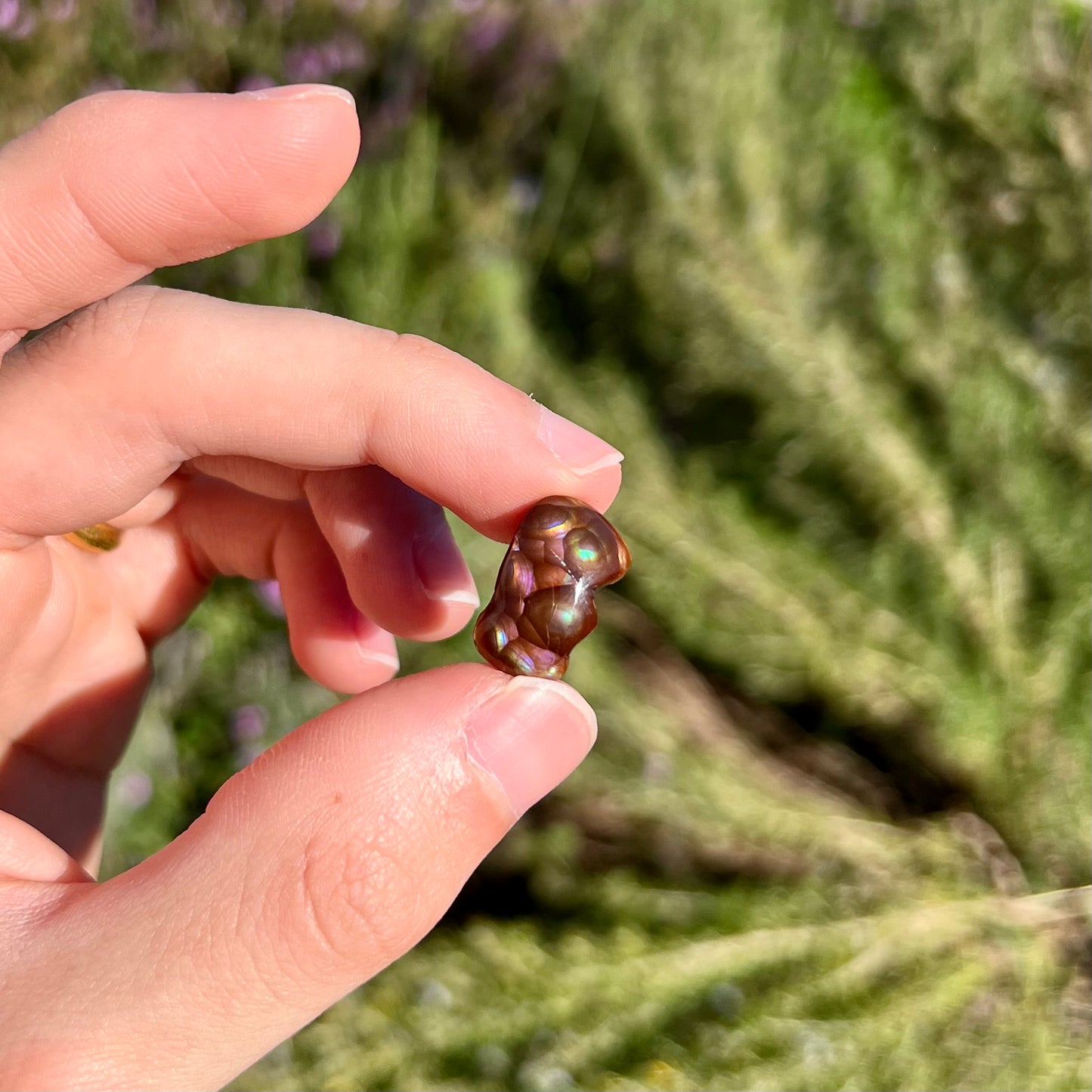 A polished, freeform shaped fire agate stone.  The stone is purple, green, and blue with red and yellow banding.