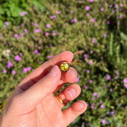 An iridescent green, yellow, and red Mexican fire agate stone.  The stone is an off-round cabochon.