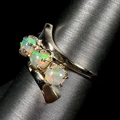 A yellow gold bypass shank ring mounted with three round cabochon cut Ethiopian fire opals.