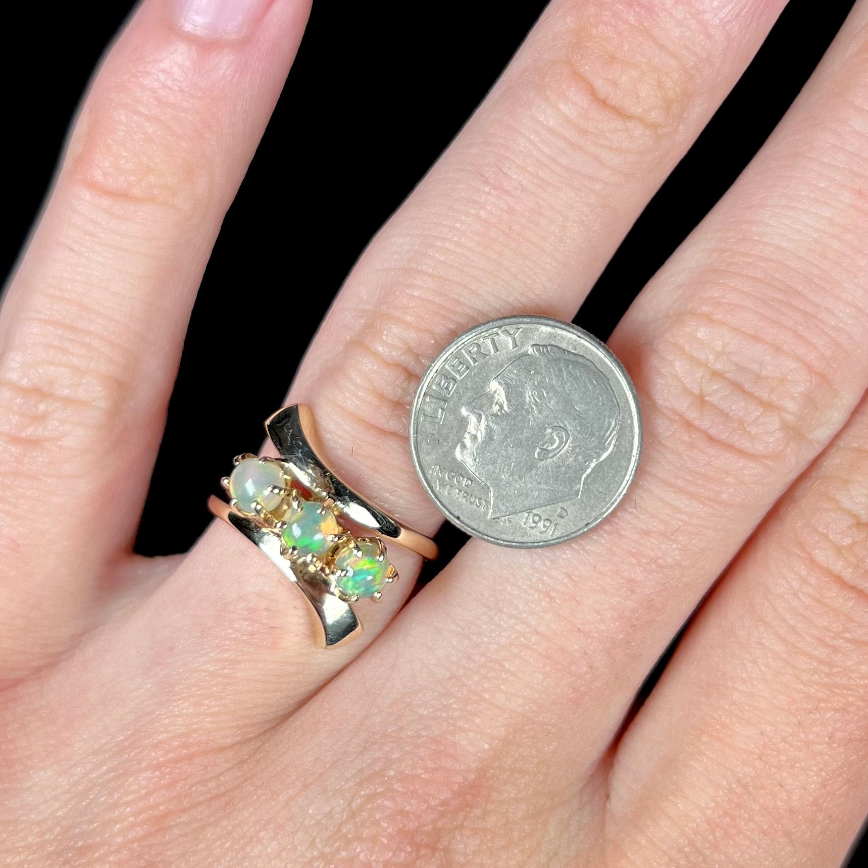 A yellow gold bypass shank ring mounted with three round cabochon cut Ethiopian fire opals.