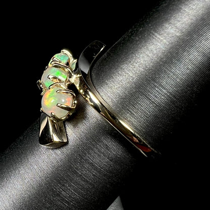 A yellow gold bypass shank ring mounted with three round cabochon cut Ethiopian fire opals.