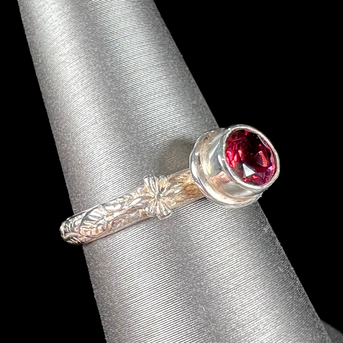 A ladies' sterling silver purple rhodonite garnet solitaire ring.  The shank has an etched floral leaf design.