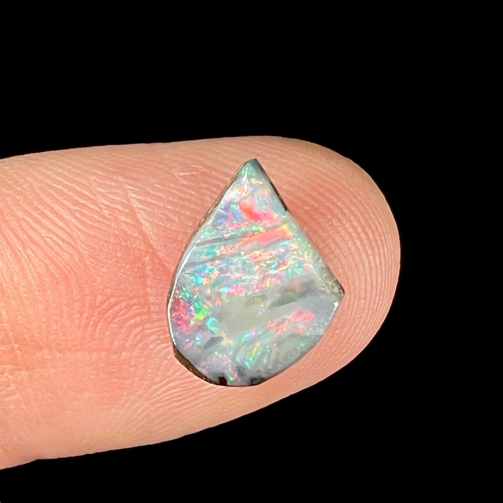 A freeform shaped boulder opal stone with red and blue color play.