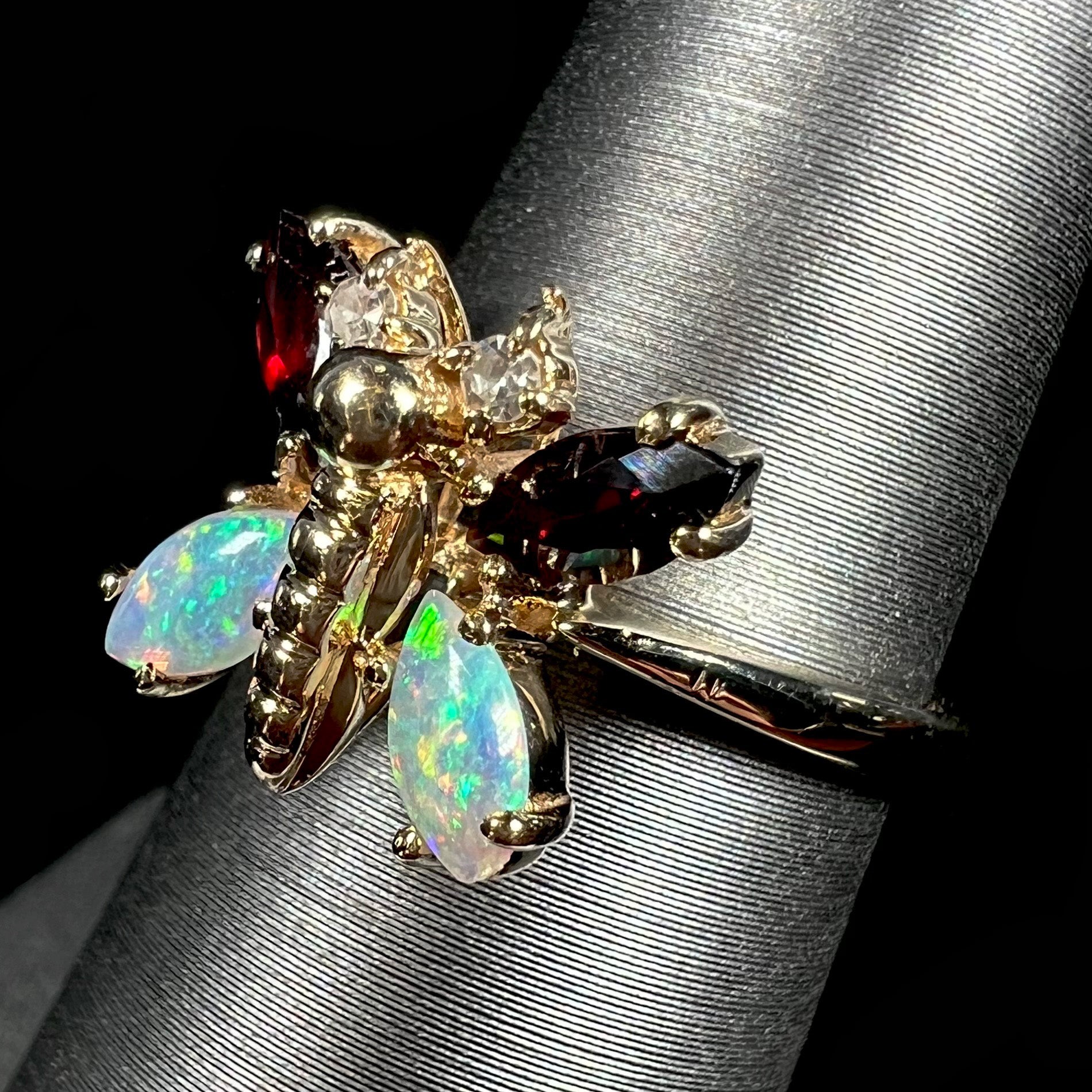 A yellow gold butterfly ring mounted with marquise cut garnets and opals and round diamond accents.