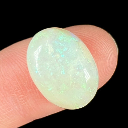 An oval cabochon cut white opal stone from Coober Pedy, Australia.  The opal has subtle colors of green and blue.