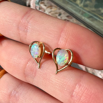 A pair of yellow gold, heart shaped stud earrings set with oval cabochon cut natural opal stones.