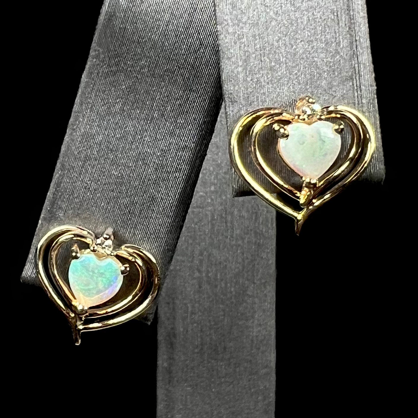 A pair of heart shaped, yellow gold opal stud earrings.  The top of the earrings have a diamond accent.