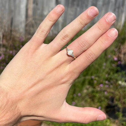 A dainty, pear shaped opal ring mounted in yellow gold with moissanite accents.