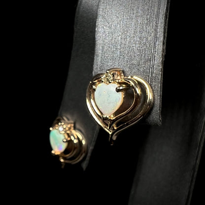 A pair of heart shaped, yellow gold opal stud earrings.  The top of the earrings have a diamond accent.