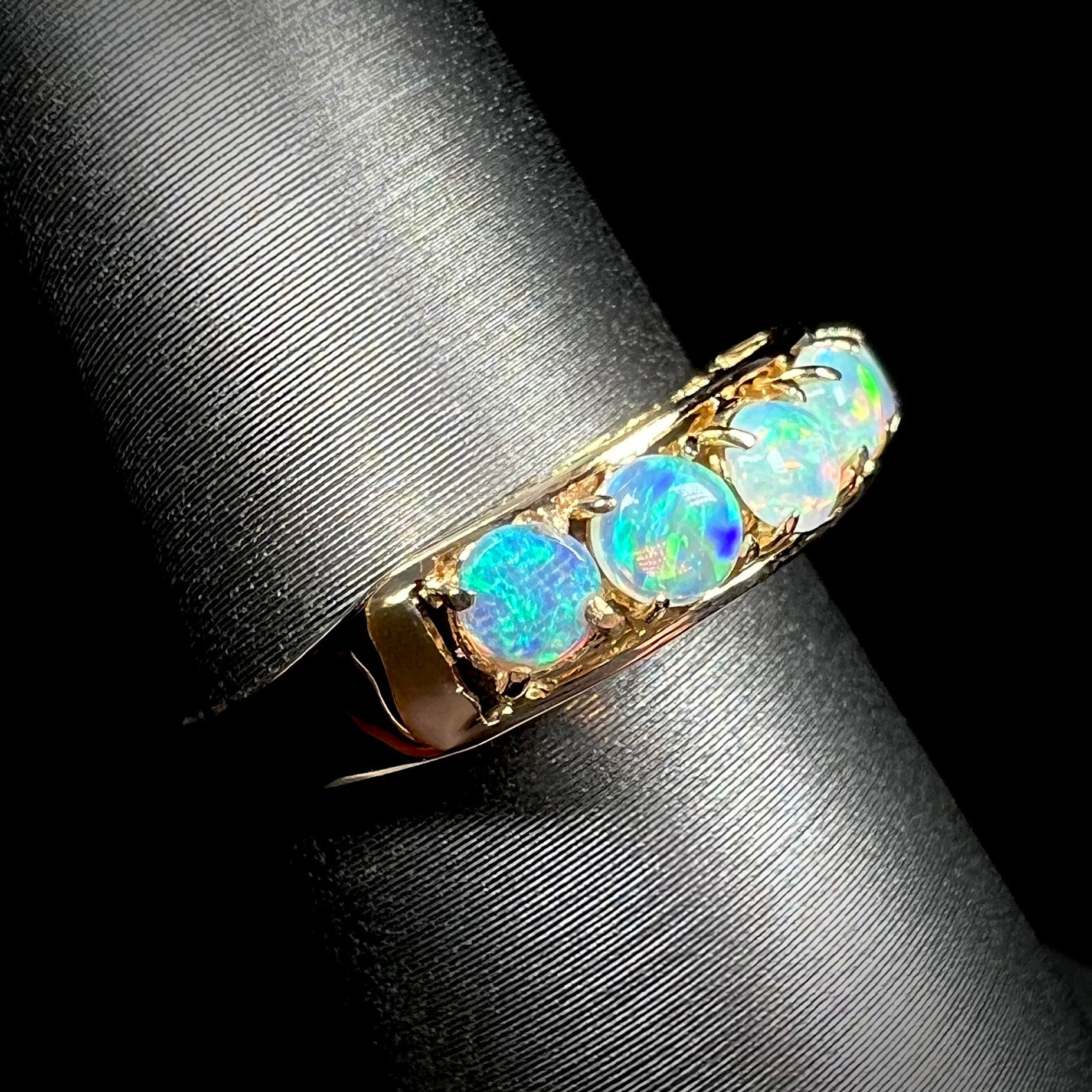 An 18 karat yellow gold line-style filigree ring mounted with five round, cabochon cut Australian crystal opals.