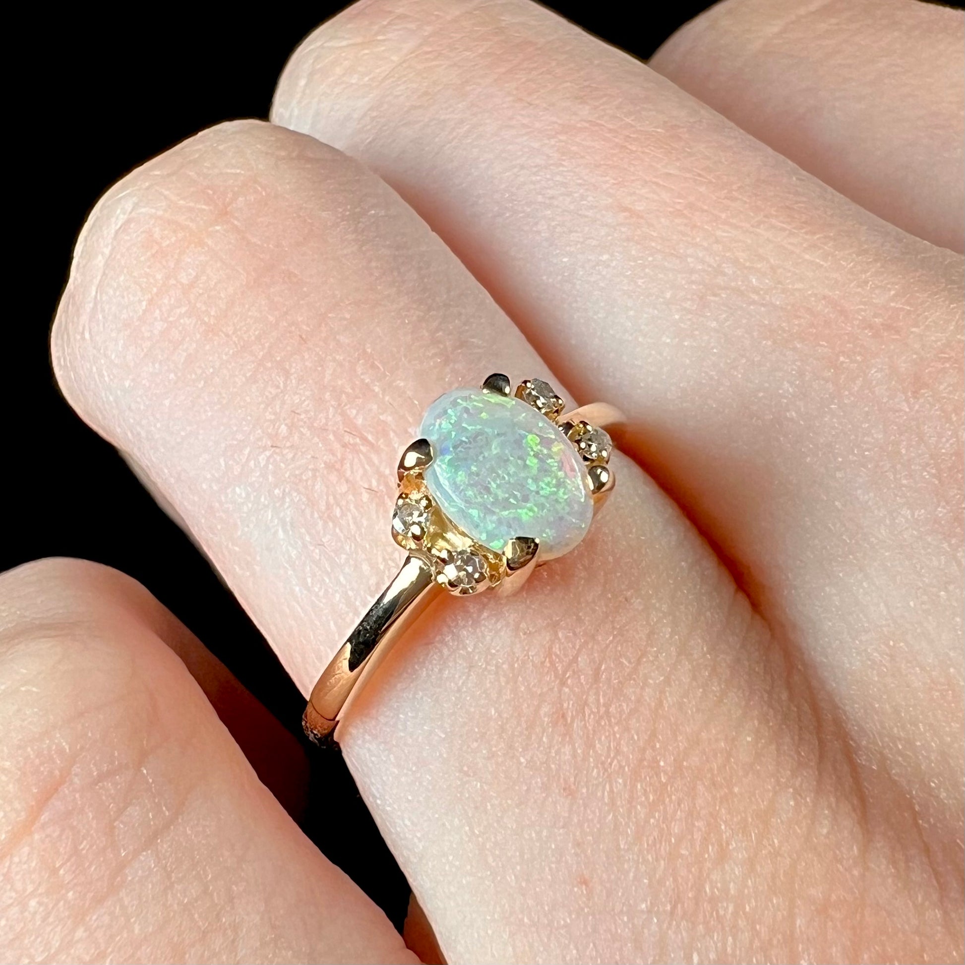 A dainty yellow gold ring set with a Coober Pedy opal with green flashfire pattern and diamond accents.