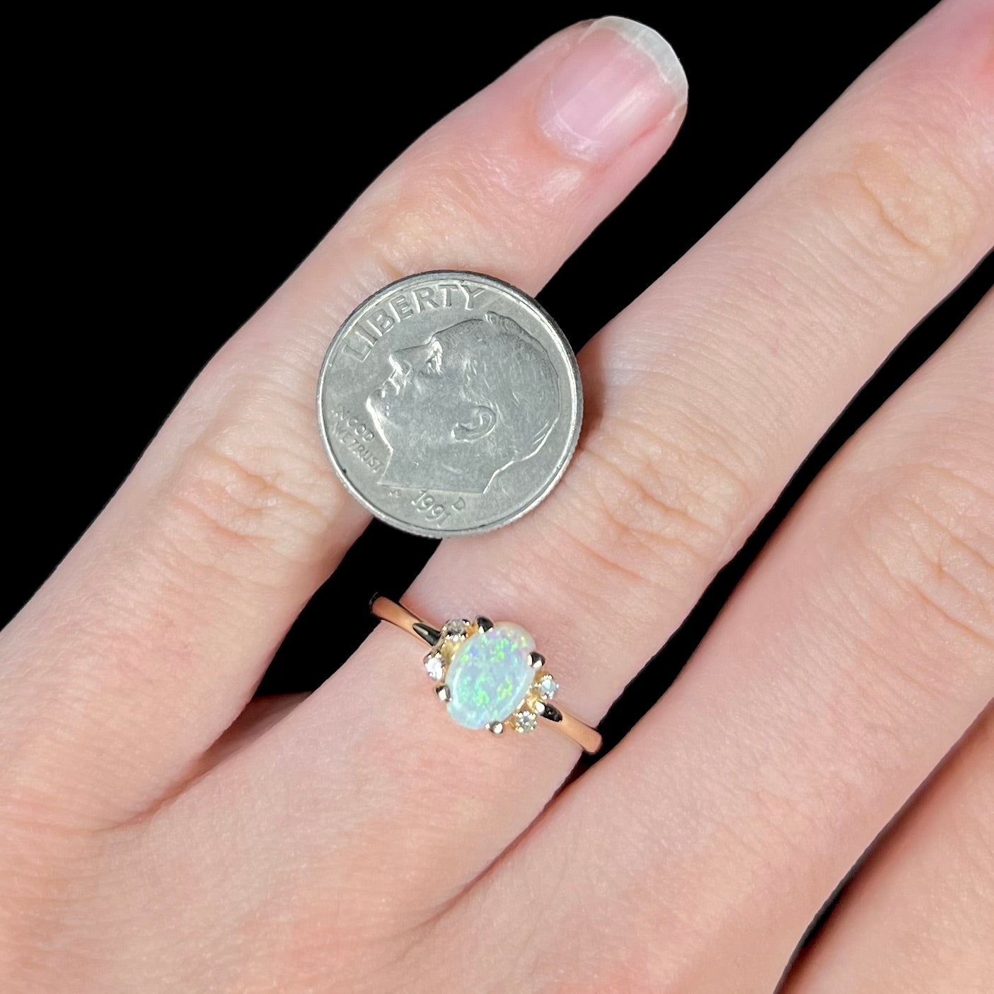 A dainty yellow gold ring set with a Coober Pedy opal with green flashfire pattern and diamond accents.