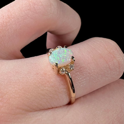 A dainty yellow gold ring set with a Coober Pedy opal with green flashfire pattern and diamond accents.