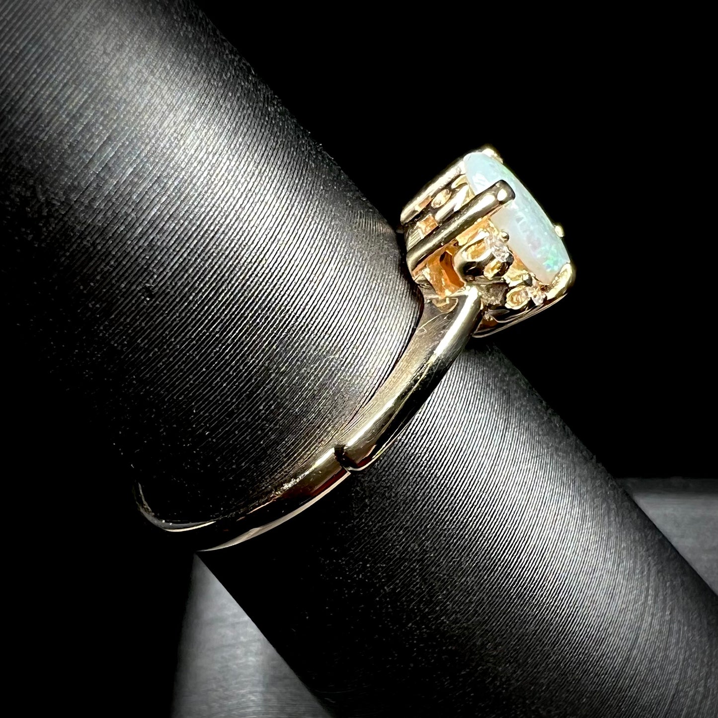 A dainty yellow gold ring set with a Coober Pedy opal with green flashfire pattern and diamond accents.