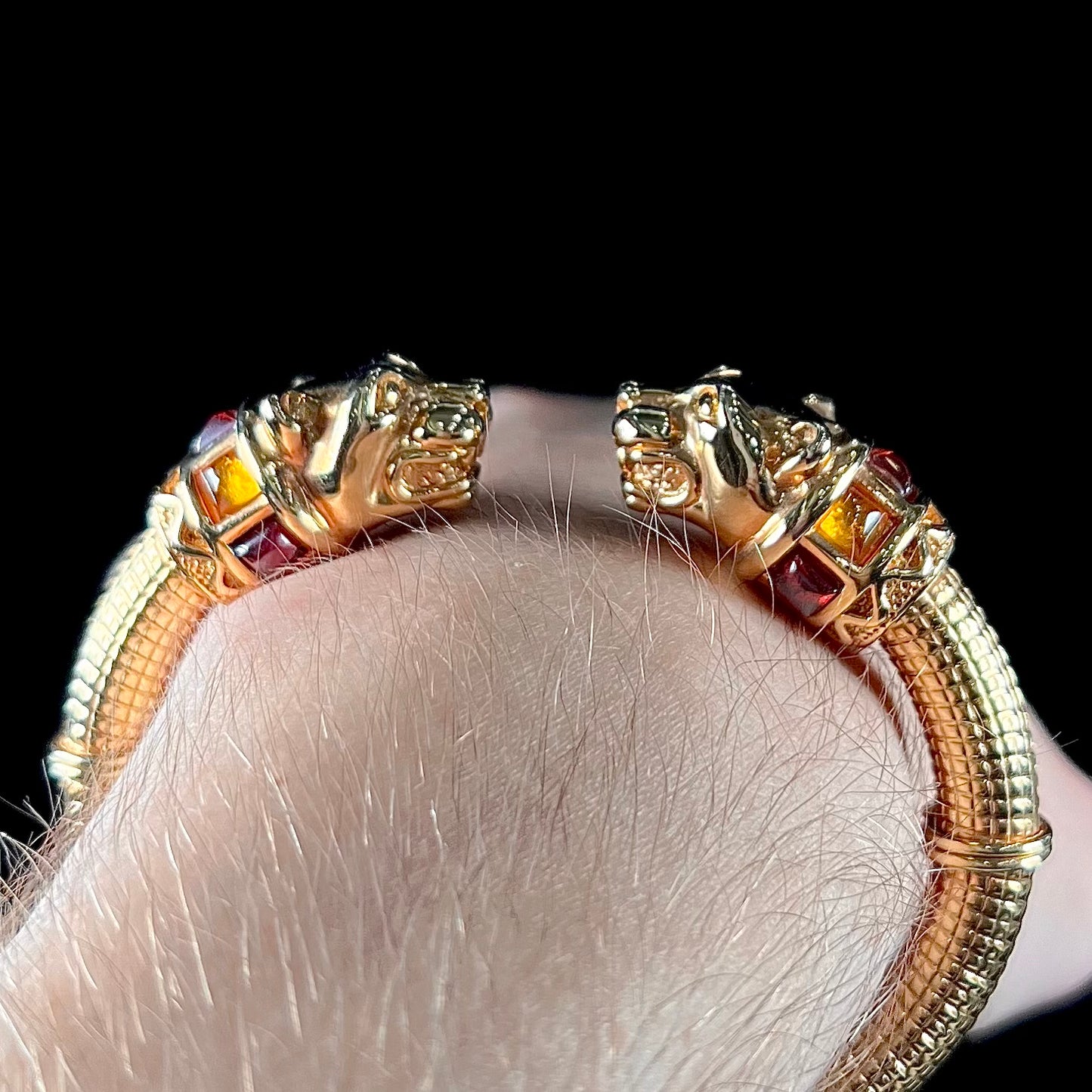 A 14 karat yellow gold hinged bangle bracelet featuring the motif of two panther heads.  There are yellow and red accent stones.