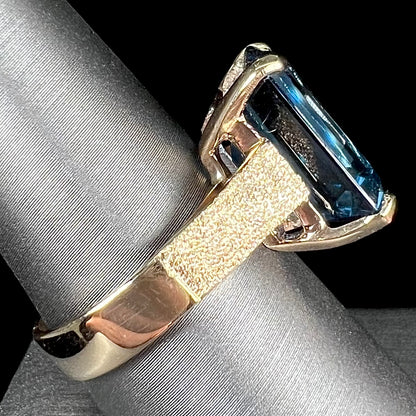 A ladies' yellow gold London blue topaz solitaire ring.  The ring is textured, and the topaz is emerald cut.