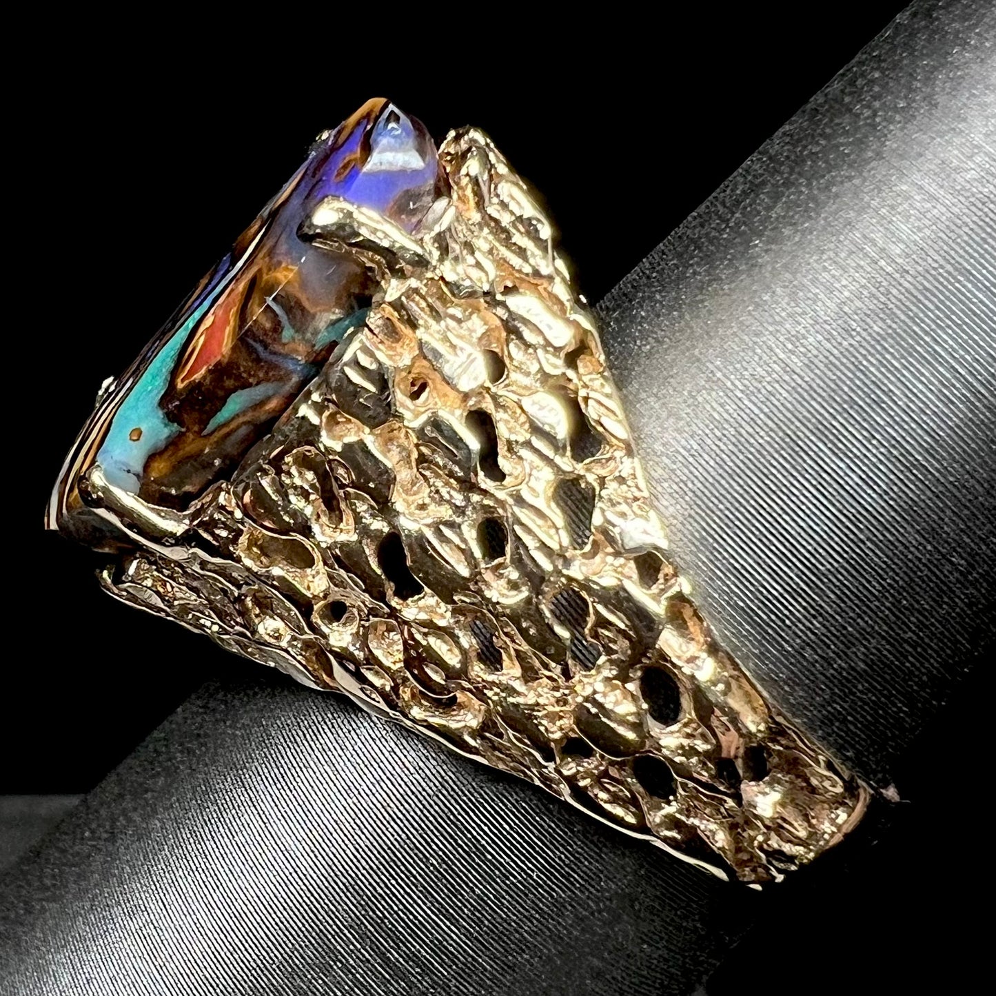 A yellow gold solitaire ring mounted with a Koroit boulder opal stone that shows the picture of a peacock.