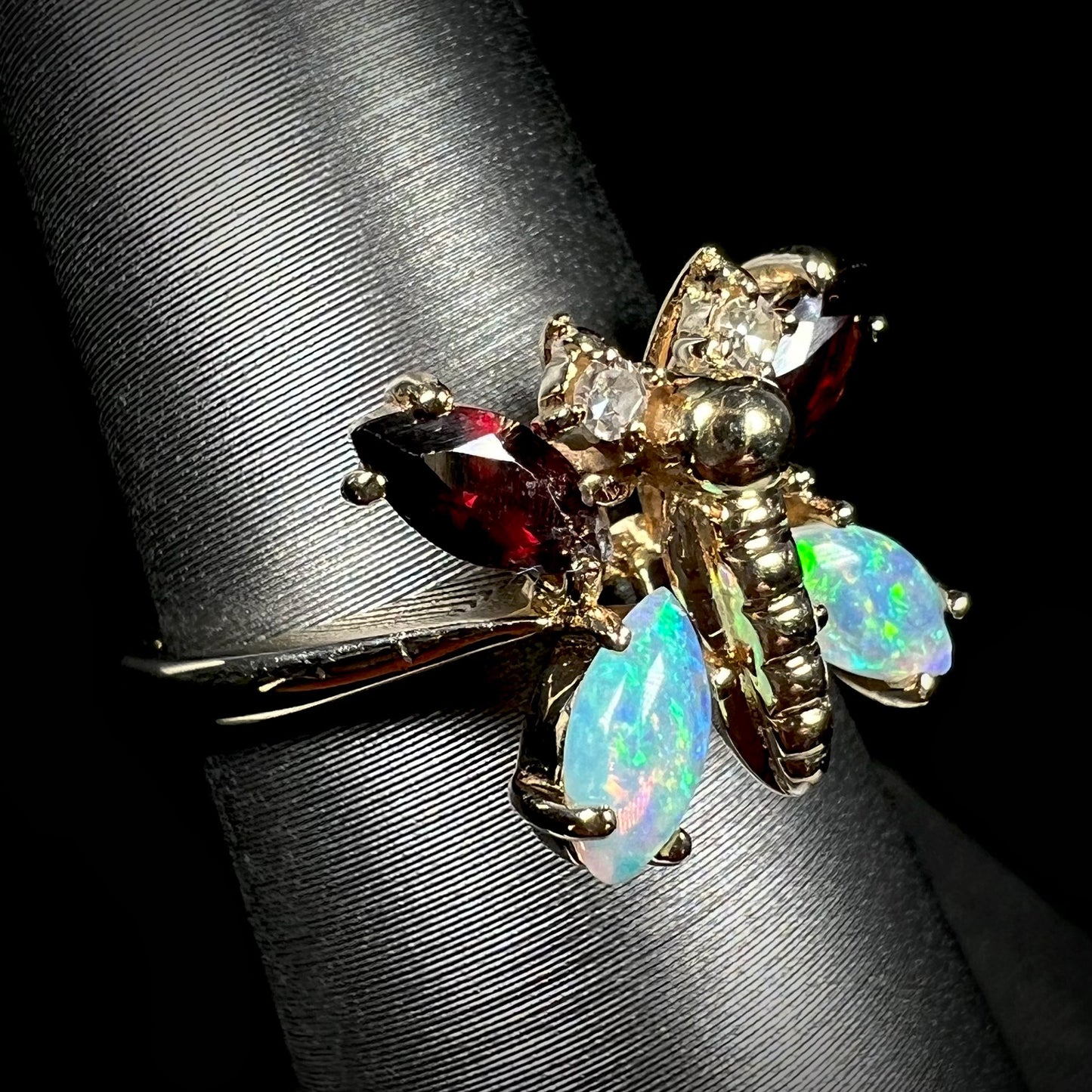 A yellow gold butterfly ring mounted with marquise cut garnets and opals and round diamond accents.