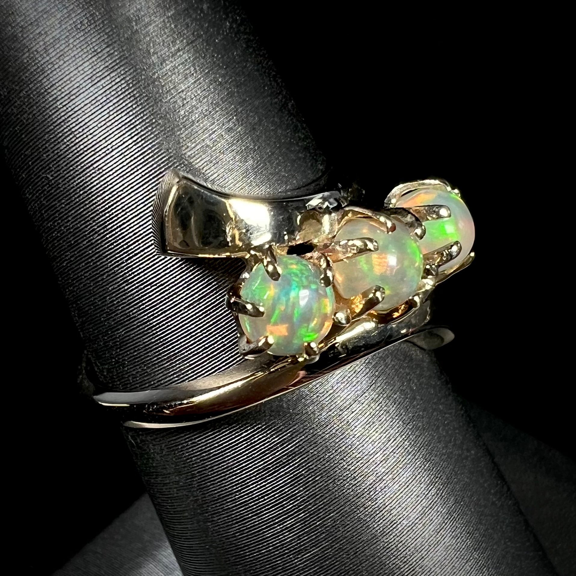 A yellow gold bypass shank ring mounted with three round cabochon cut Ethiopian fire opals.