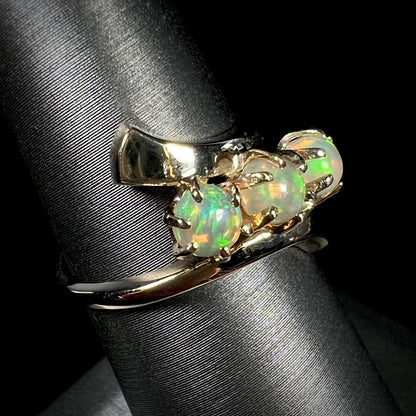 A yellow gold bypass shank ring mounted with three round cabochon cut Ethiopian fire opals.