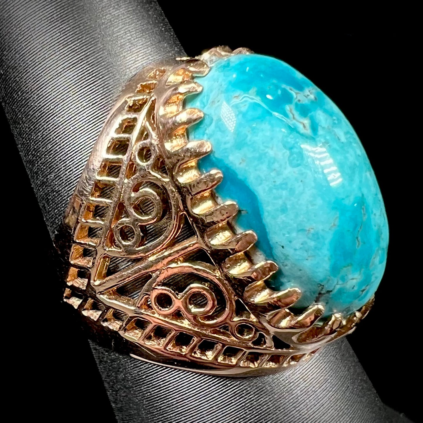 A yellow gold filigree style ring mounted with an oval Pilot Mountain turquoise stone.