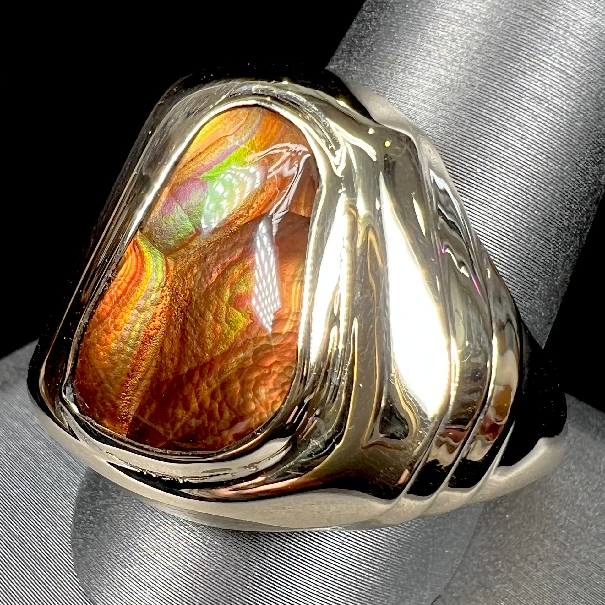 A heavy, yellow gold men's ring mounted with a Mexican fire agate stone.  The fire agate has orange, green, red, and purple colors.