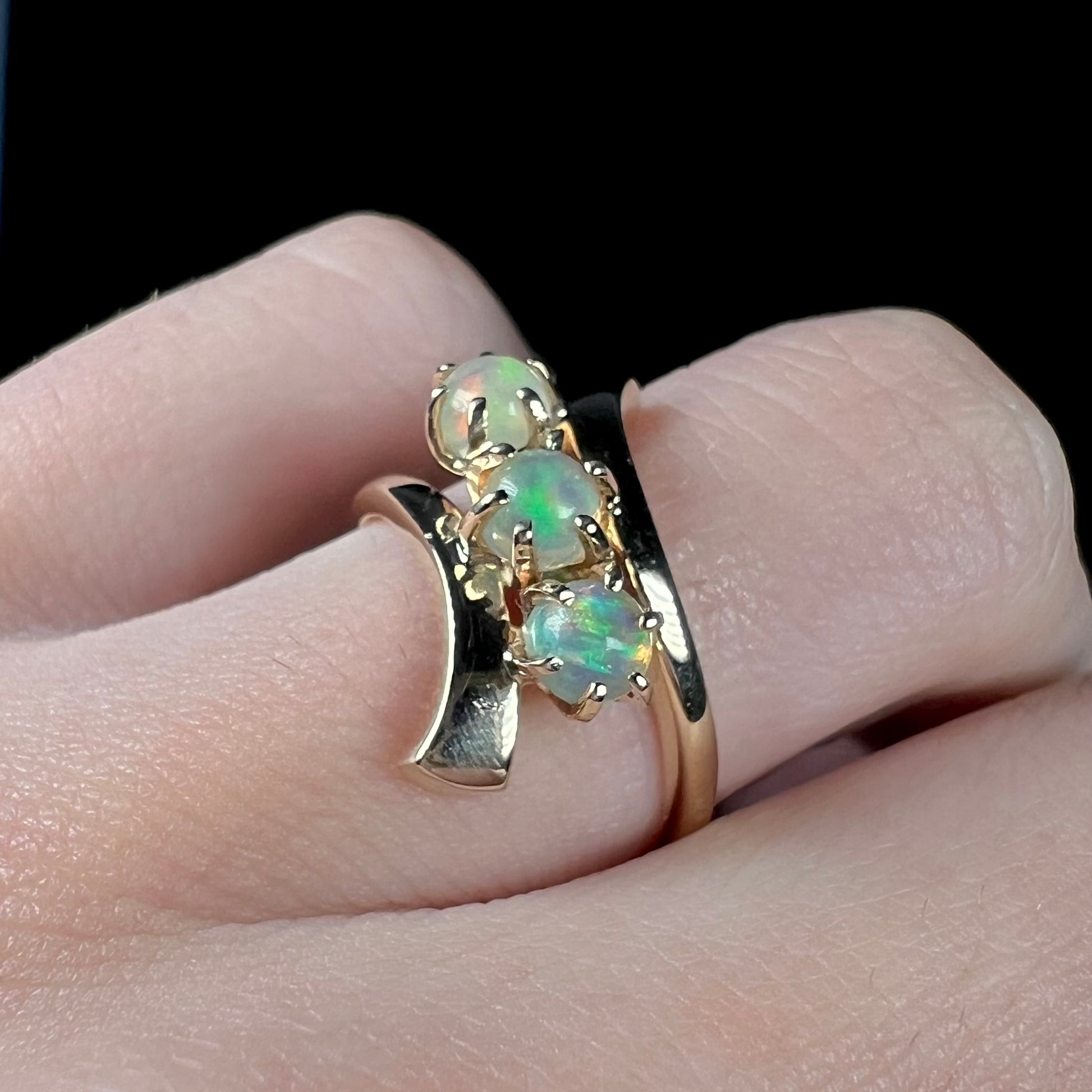 A yellow gold bypass shank ring mounted with three round cabochon cut Ethiopian fire opals.