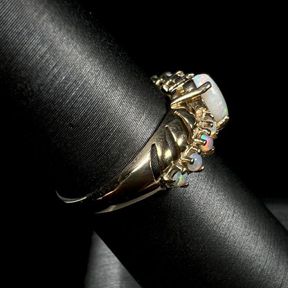 A yellow gold ring featuring two crossing, alternating lines of round cut synthetic opals.  In the middle is a larger oval cut synthetic opal.