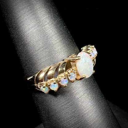 A yellow gold ring featuring two crossing, alternating lines of round cut synthetic opals.  In the middle is a larger oval cut synthetic opal.