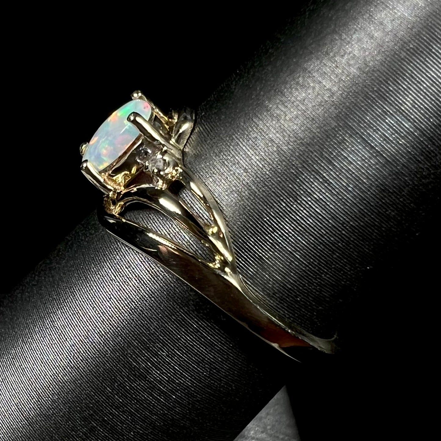 A yellow gold ring mounted with two diamond accents and an oval cut lab created opal.  The opal has bright red colors.