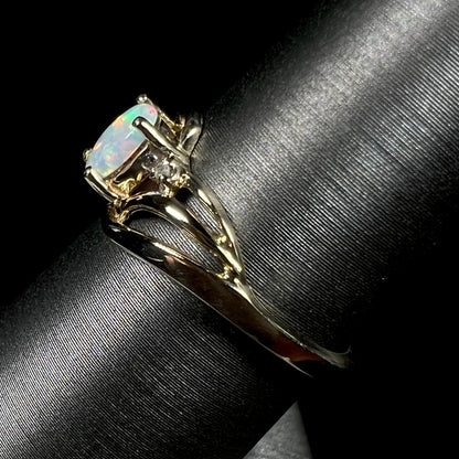 A yellow gold ring mounted with two diamond accents and an oval cut lab created opal.  The opal has bright red colors.