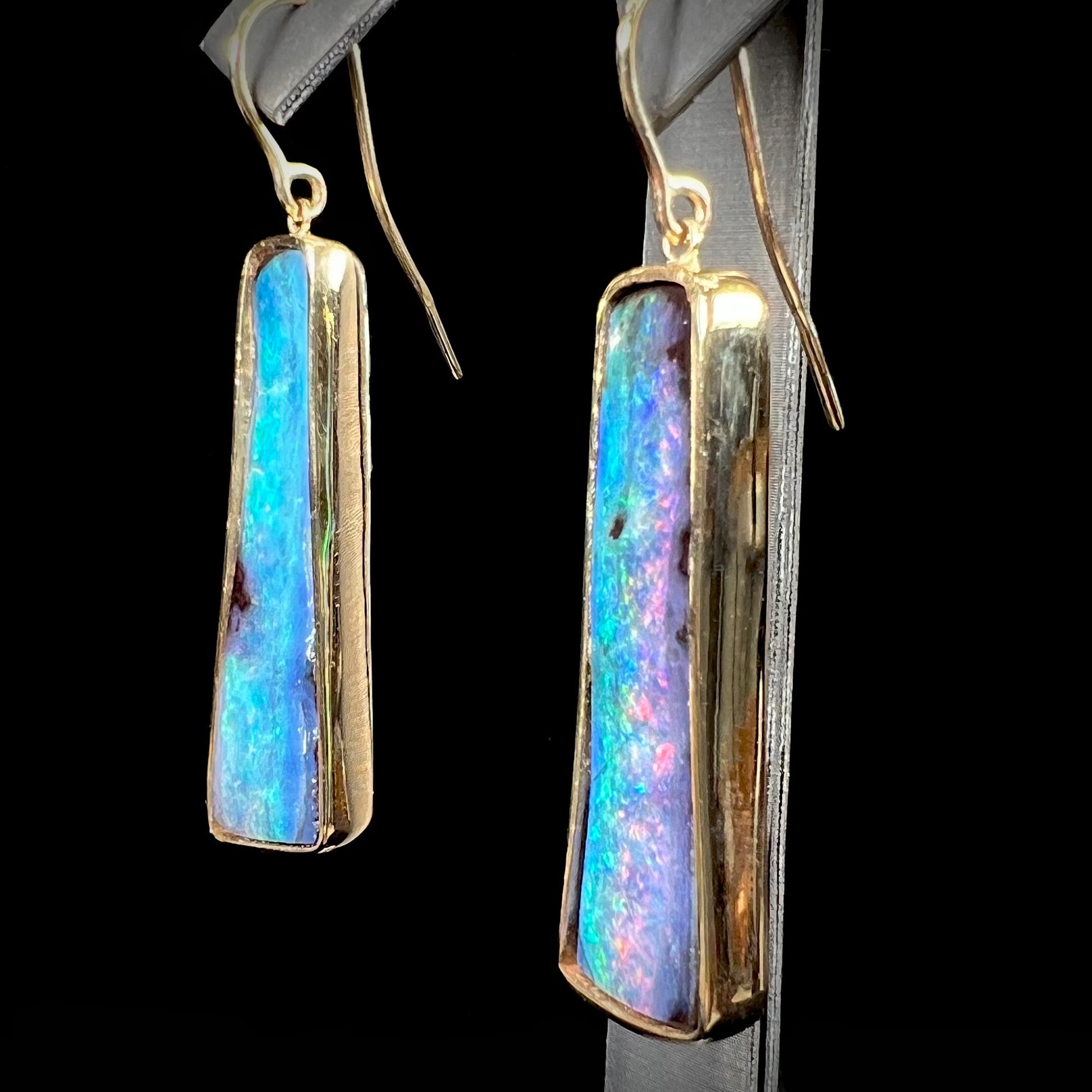 A pair of natural boulder opal dangle earrings set in yellow gold.  The opal displays a rainbow of colors and is from Bull Creek, Australia.