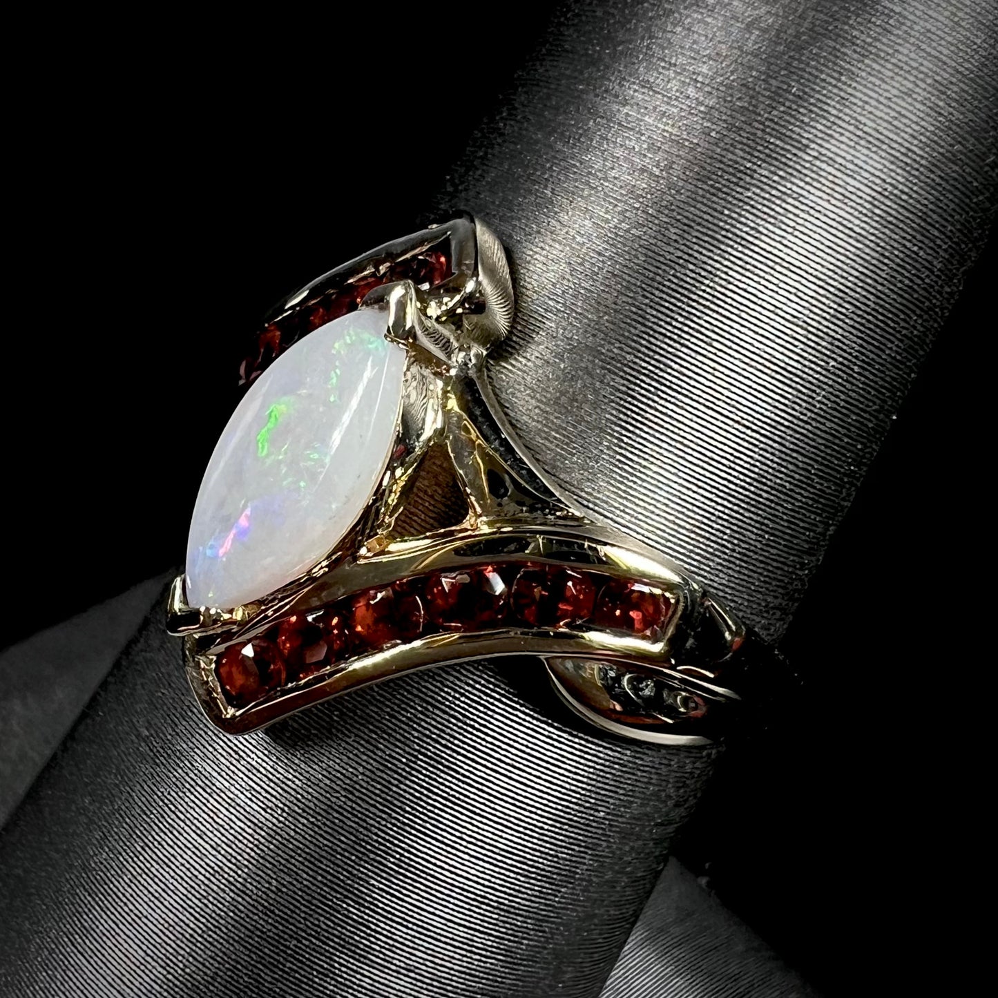 A marquise cut white opal ring.  The ring is accented with channel set reddish orange garnets.