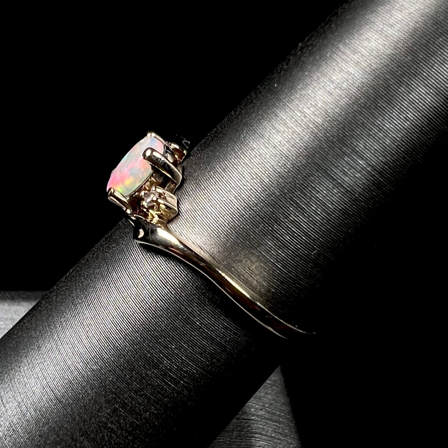 A dainty yellow gold opal and diamond-accented ring.  The opal has red and purple colors.